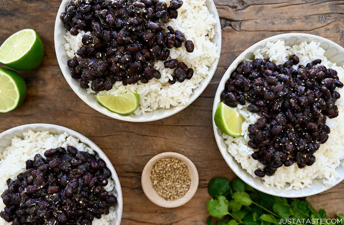 Three bowls containing white rice topped with Cuban black beans and a lime wedge.