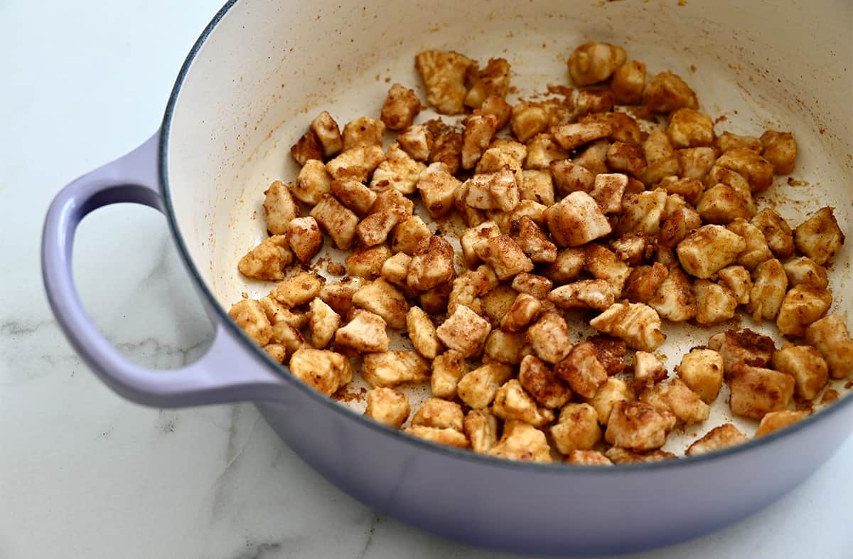 Sautéed chicken pieces in a large lavender stockpot.