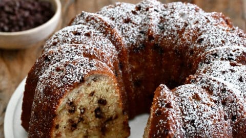 A banana chocolate chip bundt cake with one slice missing, dusted with powdered sugar.