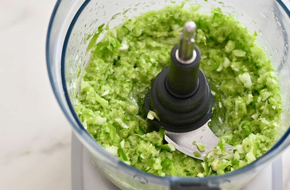 A food processor bowl containing sofrito, which is a mix of green bell pepper, onion and garlic.