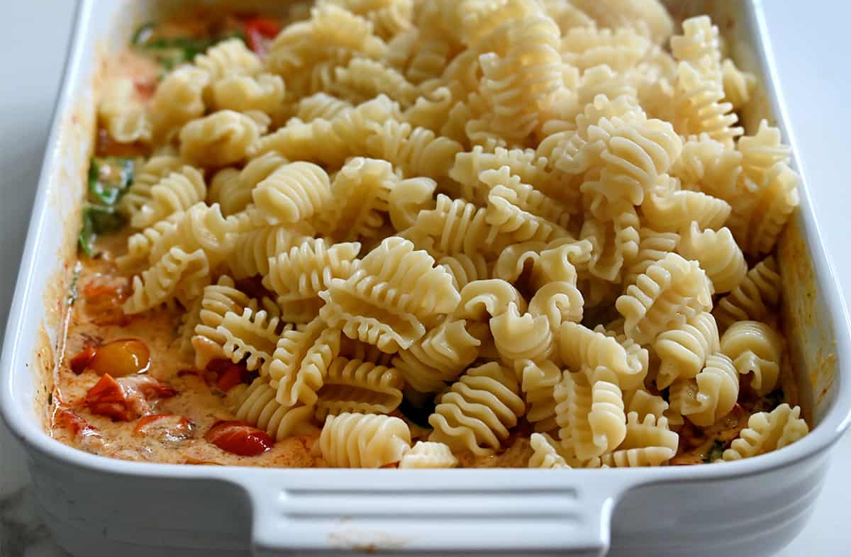 Radiatori noodles over roasted tomatoes mixed with cheese in a white baking dish.