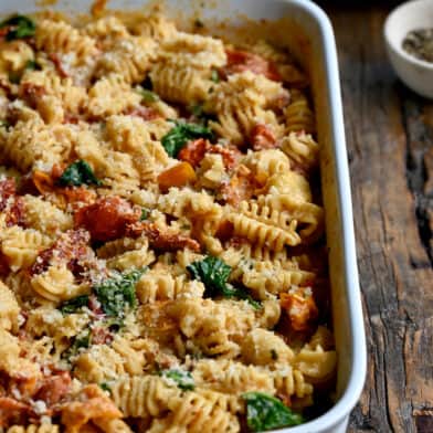 A white baking dish containing Baked Boursin Cheese Pasta with Sundried Tomatoes and Spinach sprinkled with parmesan cheese.