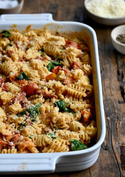 A white baking dish containing Baked Boursin Cheese Pasta with Sundried Tomatoes and Spinach sprinkled with parmesan cheese.