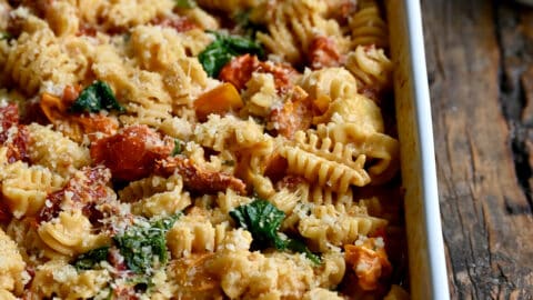 A white baking dish containing Baked Boursin Cheese Pasta with Sundried Tomatoes and Spinach sprinkled with parmesan cheese.