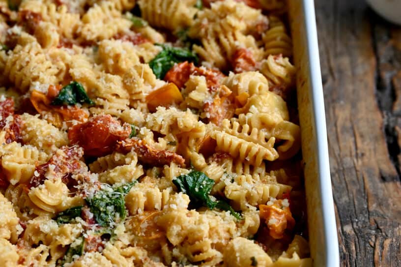 A white baking dish containing Baked Boursin Cheese Pasta with Sundried Tomatoes and Spinach sprinkled with parmesan cheese.