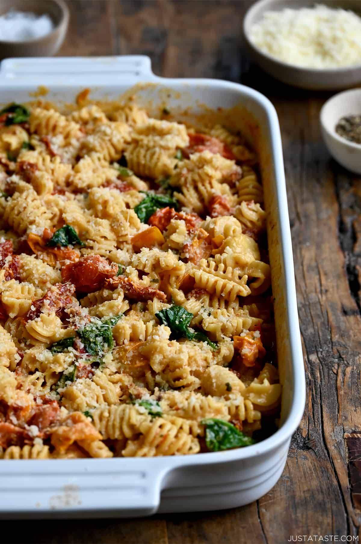 A white baking dish containing Baked Boursin Cheese Pasta with Sundried Tomatoes and Spinach sprinkled with parmesan cheese.