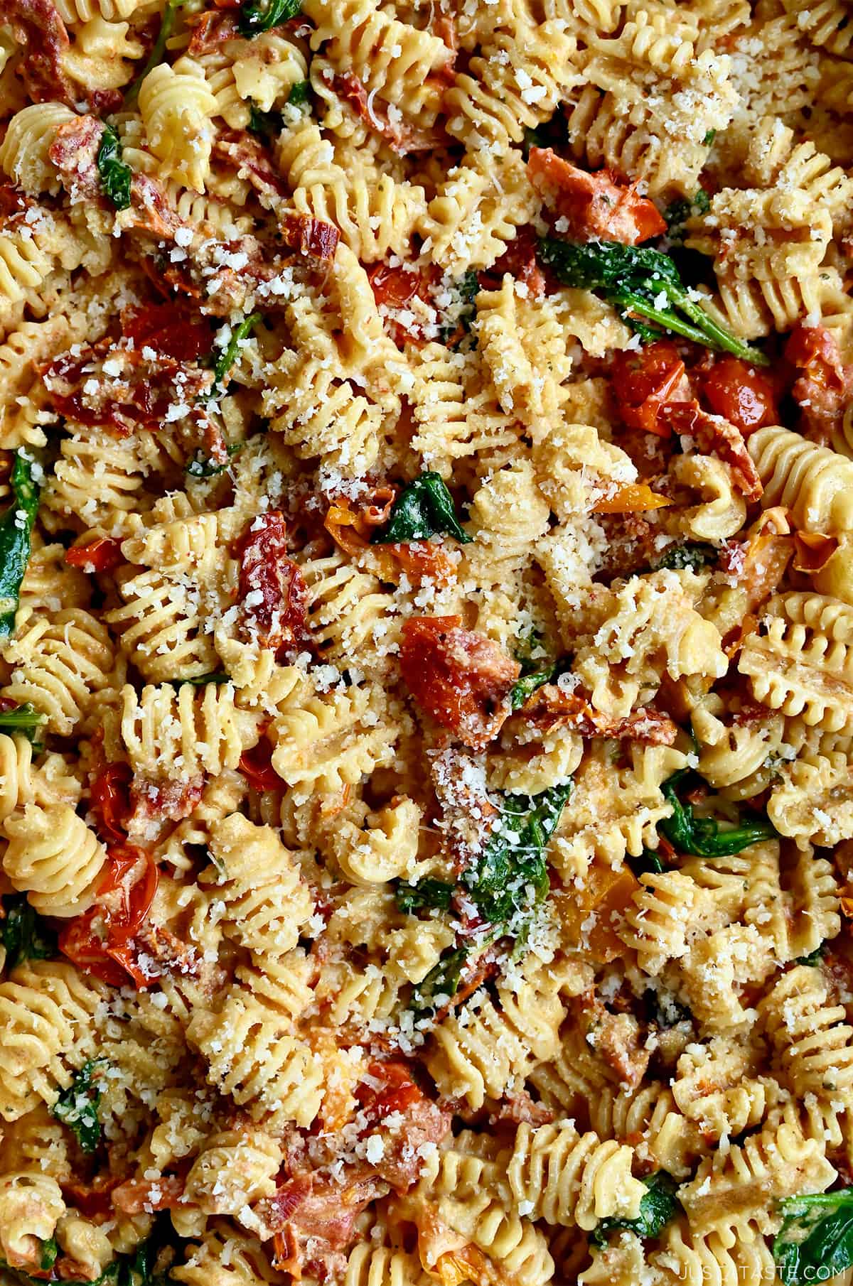 A close-up view of short pasta noodles with sun-dried tomatoes, roasted cherry tomatoes and spinach garnished with parmesan cheese.