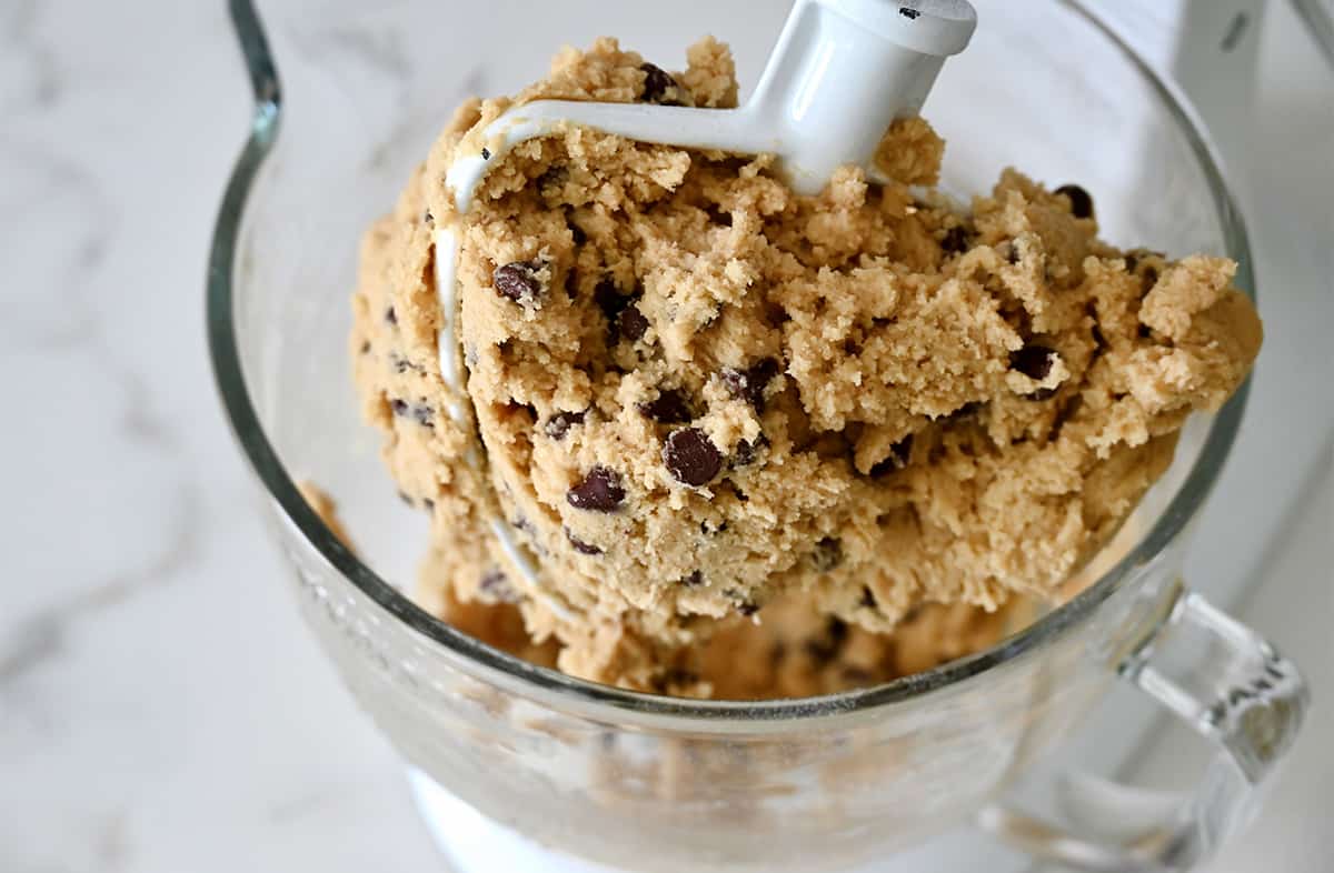 A large stand mixer bowl and paddle attached with cookie dough batter.