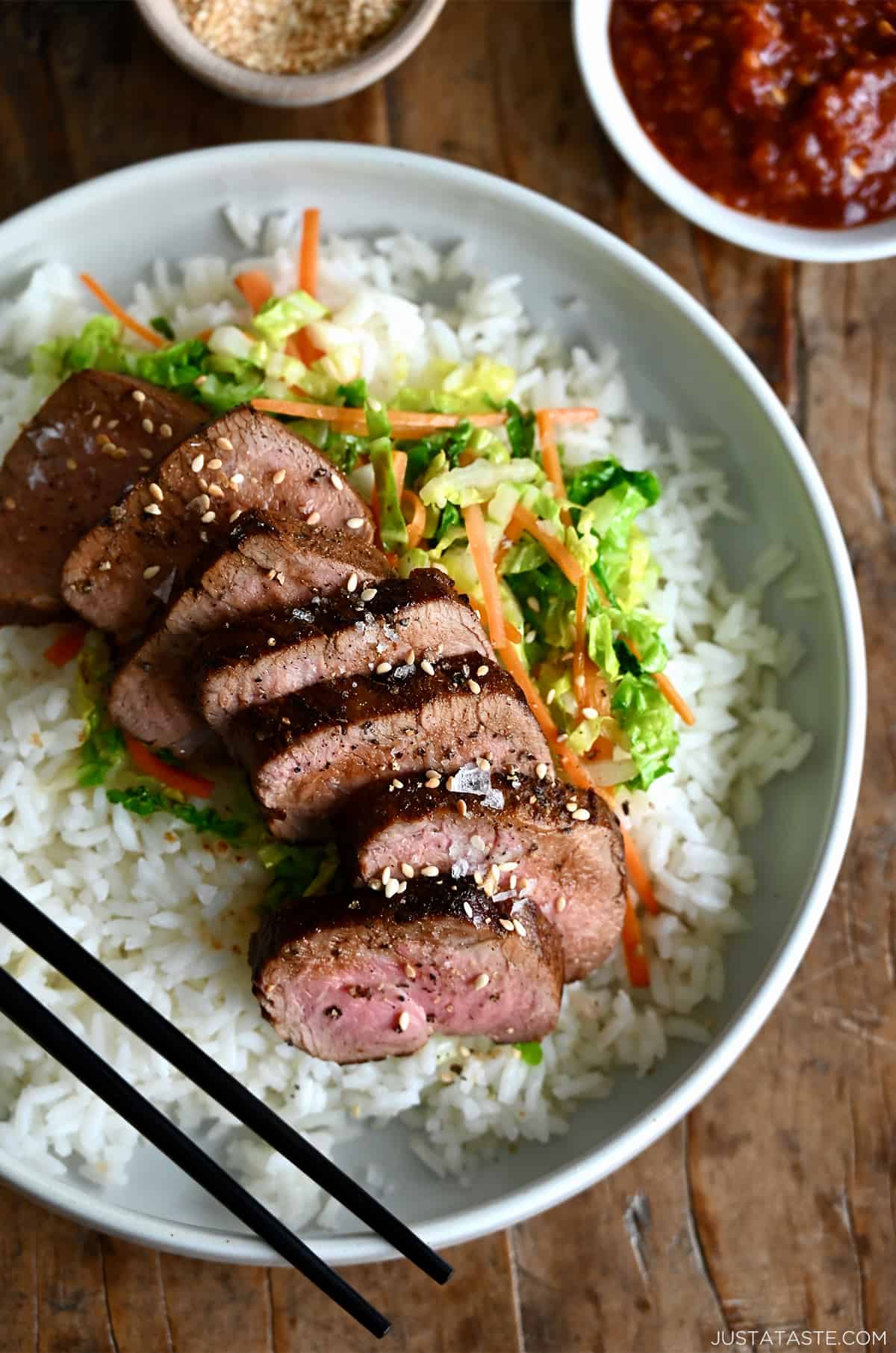 Sliced pork tenderloin over veggies and a bed of rice on a dinner plate with chopsticks.