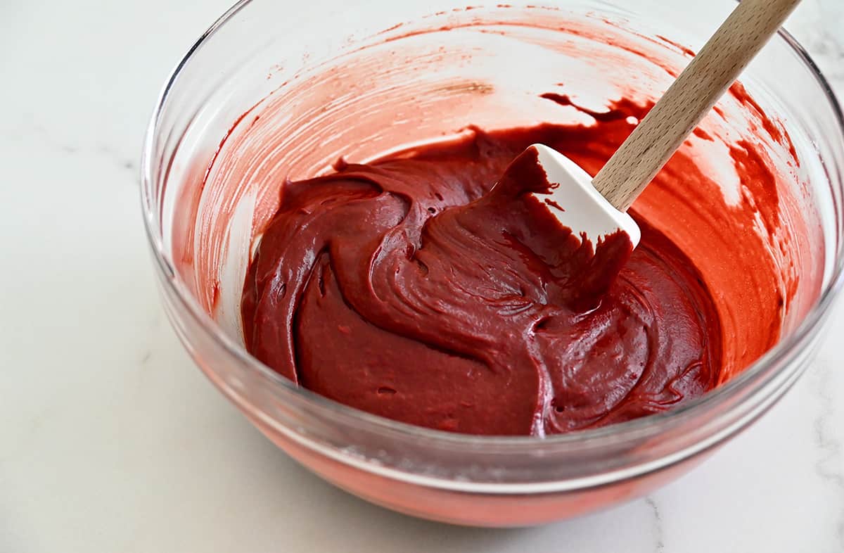 Red velvet brownie batter in a large clear bowl with a spatula.