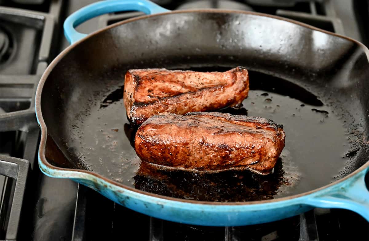 Two seared pork tenderloins in a large cast-iron skillet.