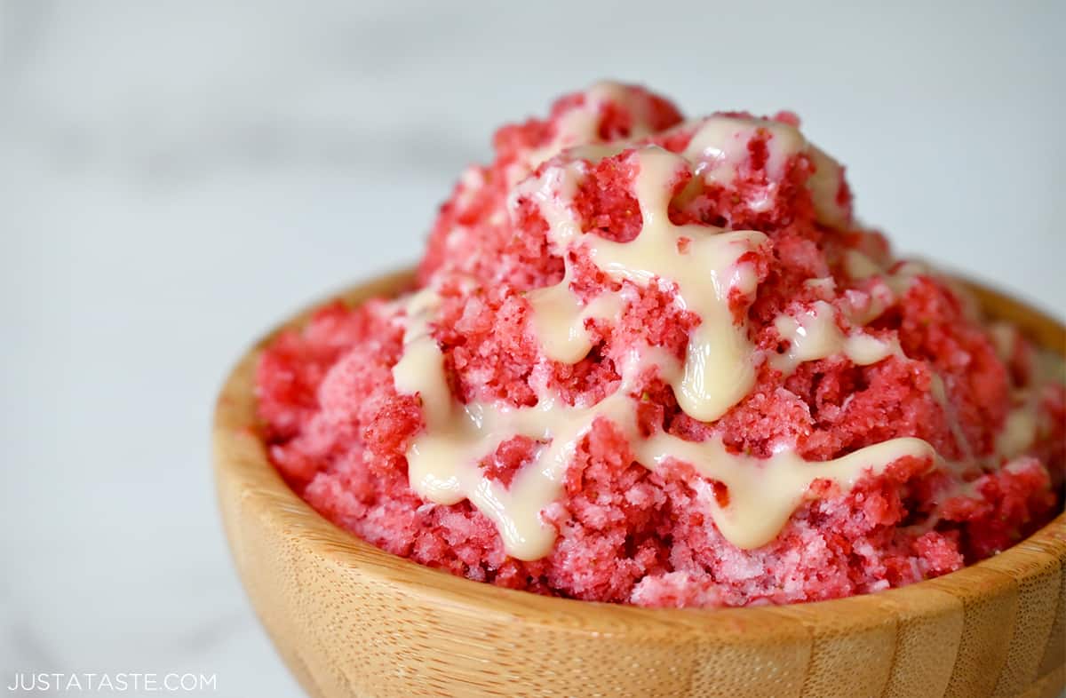 A wood bowl containing strawberry shaved ice with sweetened condensed milk drizzled on top