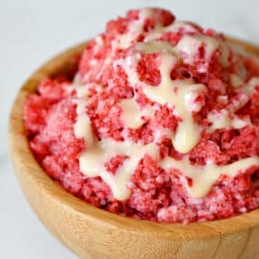 A wood bowl containing strawberry shaved ice with drizzled sweetened condensed milk