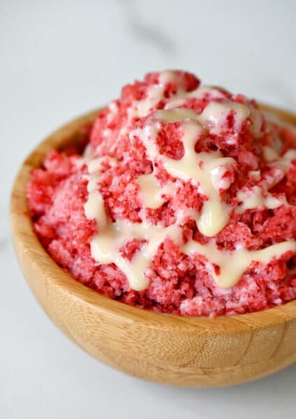 A wood bowl containing strawberry shaved ice with drizzled sweetened condensed milk