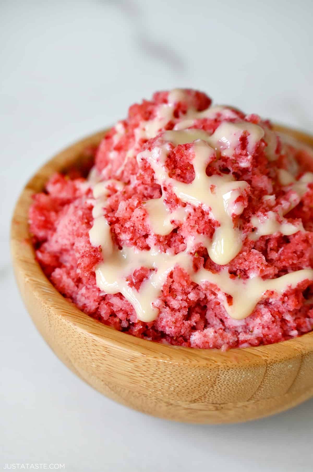 A wood bowl containing strawberry shaved ice with drizzled sweetened condensed milk