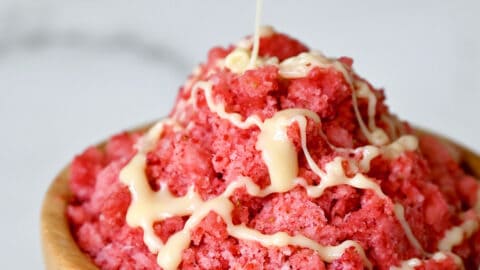 A wood bowl containing strawberry shaved ice with a drizzle of sweetened condensed milk