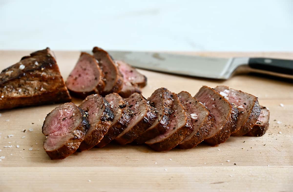 Sliced pork tenderloin on a wood cutting board with a sharp knife.