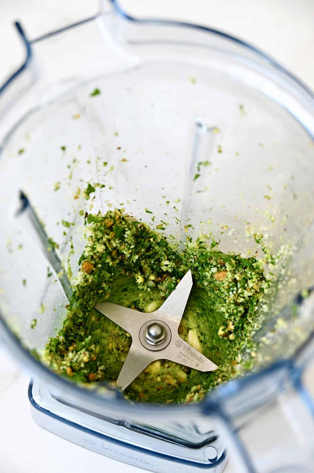Finely chopped pesto ingredients in a blender before streaming in olive oil.