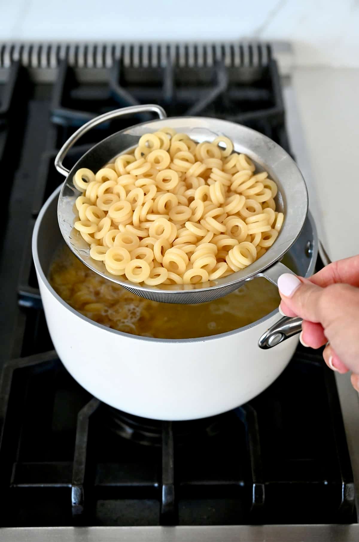 Cooked pasta in a mesh sieve over a pot of boiling water.
