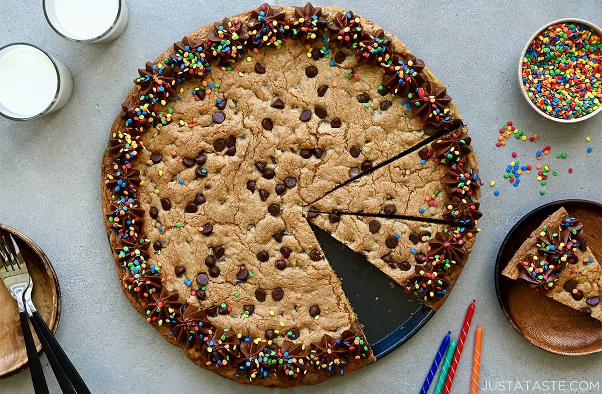 A top-down view of a chocolate chip cookie cake decorated with chocolate frosting and sprinkles next to birthday candles.