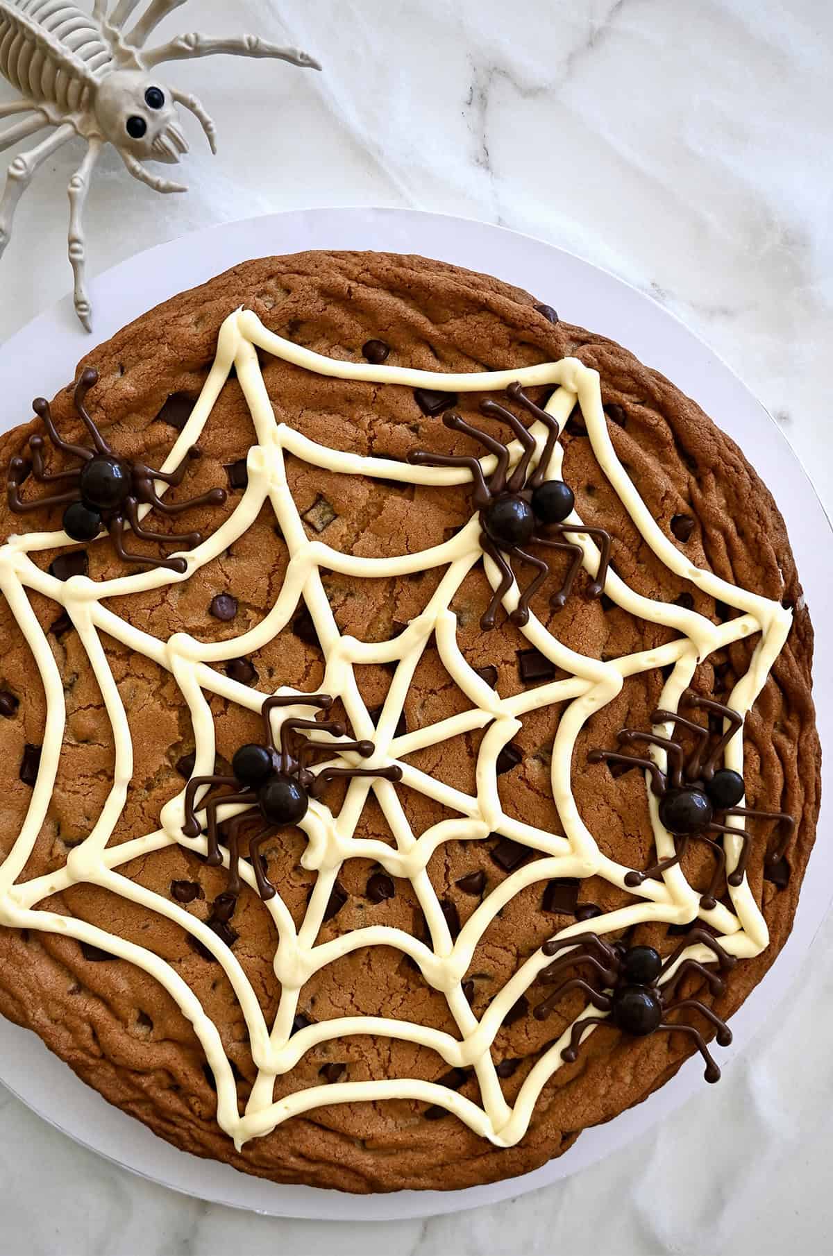 A Halloween Cookie Cake featuring a vanilla buttercream spider web with edible chocolate spiders