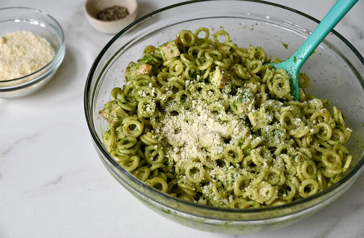 Ring-shaped pasta tossed with basil pesto in a clear bowl topped with Parmesan cheese.