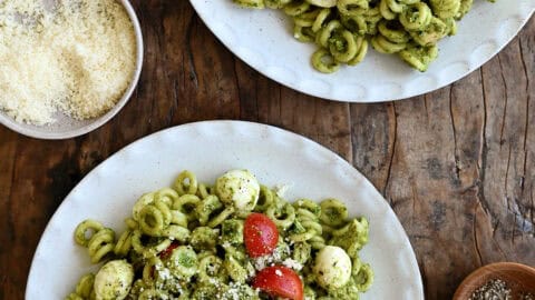 Two dinner plates with pesto pasta salad with chicken, cherry tomatoes and mini mozzarella balls.