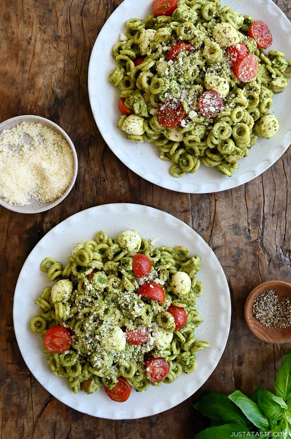 Two dinner plates with pesto pasta salad with chicken, cherry tomatoes and mini mozzarella balls.