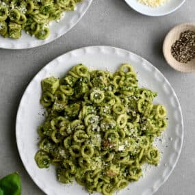 A top-down view of a plate topped with pesto pasta with chicken garnished with Parmesan cheese.