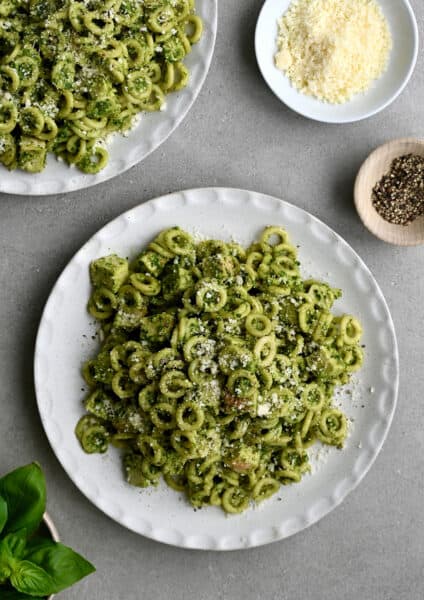 A top-down view of a plate topped with pesto pasta with chicken garnished with Parmesan cheese.