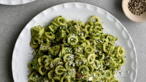 A top-down view of a plate topped with pesto pasta with chicken garnished with Parmesan cheese.