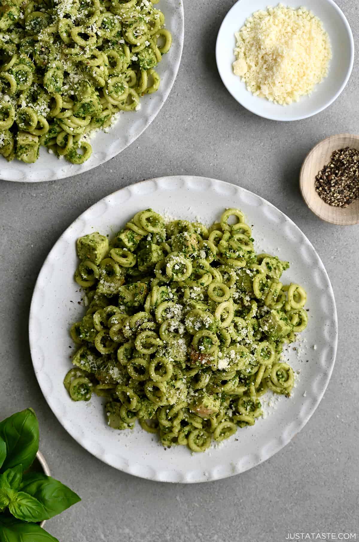 A top-down view of a plate topped with pesto pasta with chicken garnished with Parmesan cheese.