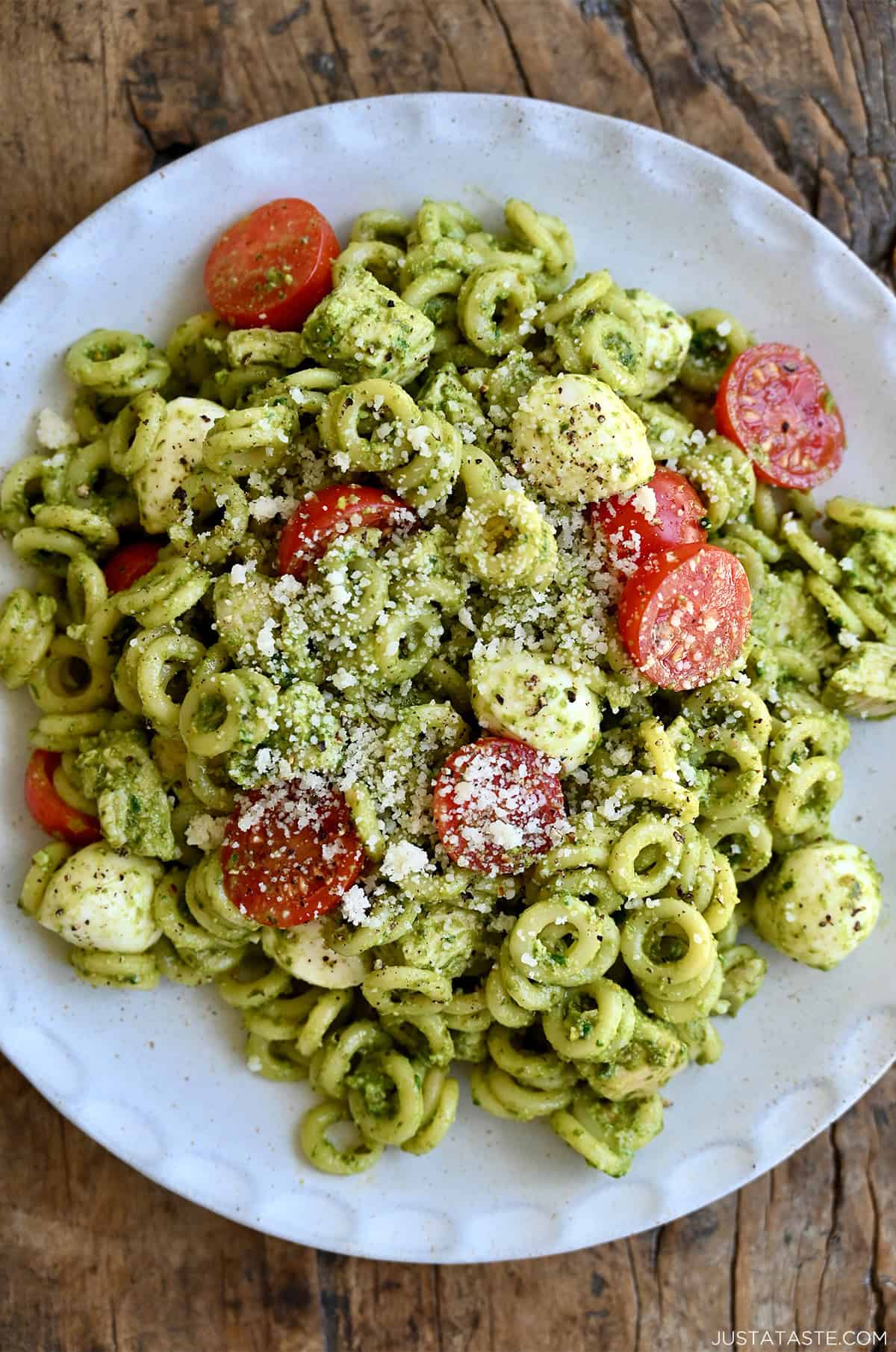 A closeup of pesto pasta salad with chicken, cherry tomatoes and mini mozzarella balls.