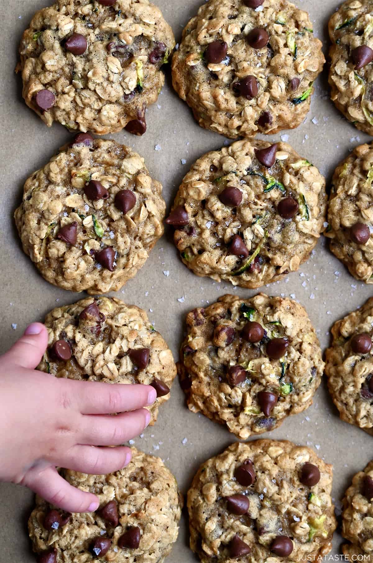 A child's hand reaches for a zucchini oatmeal chocolate chip cookie.