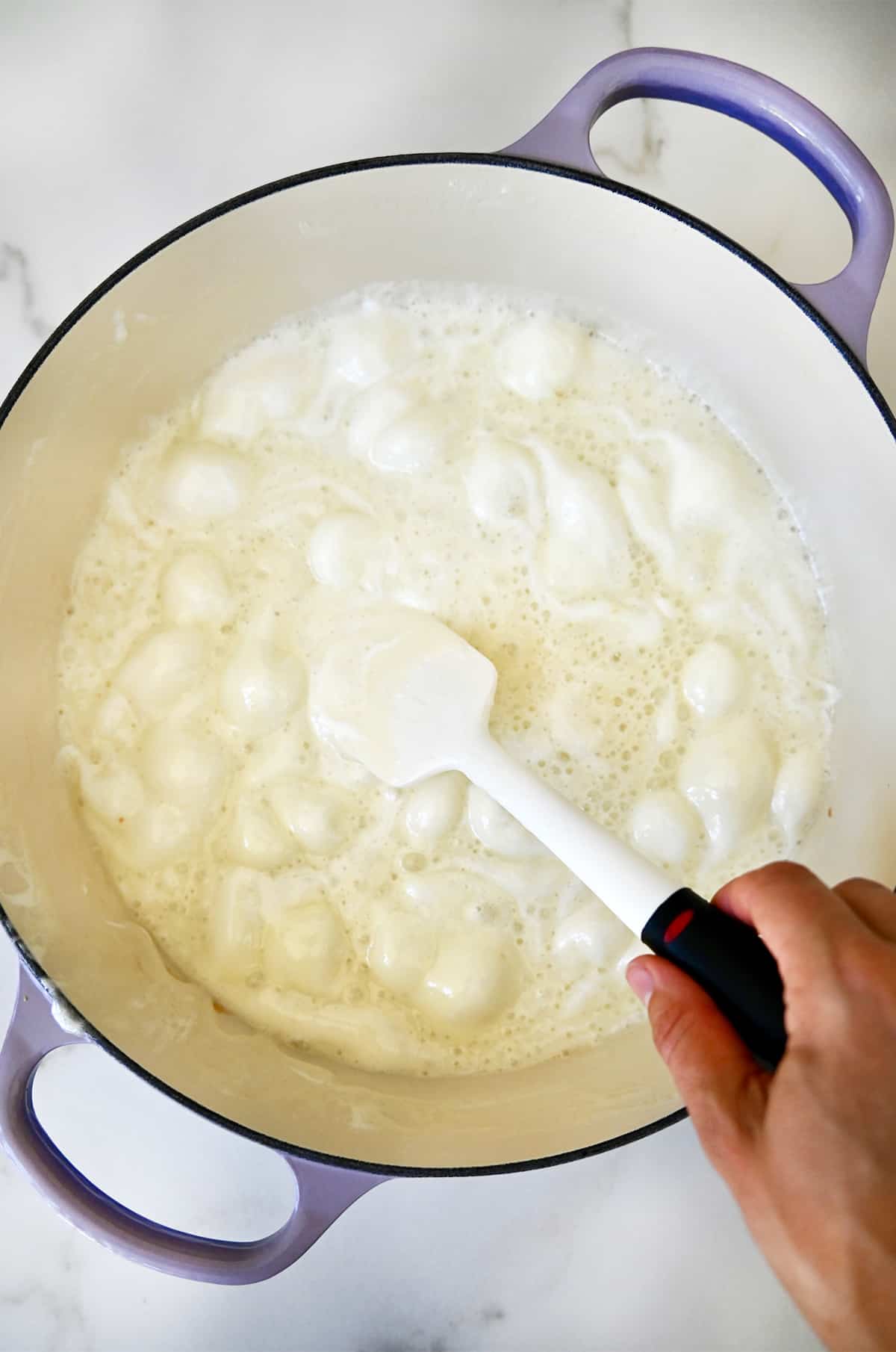 A hand holds a spatula into a large stockpot with melted marshmallows.