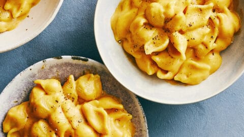 Two bowls containing creamy pumpkin macaroni and cheese next to a small bowl containing black pepper.