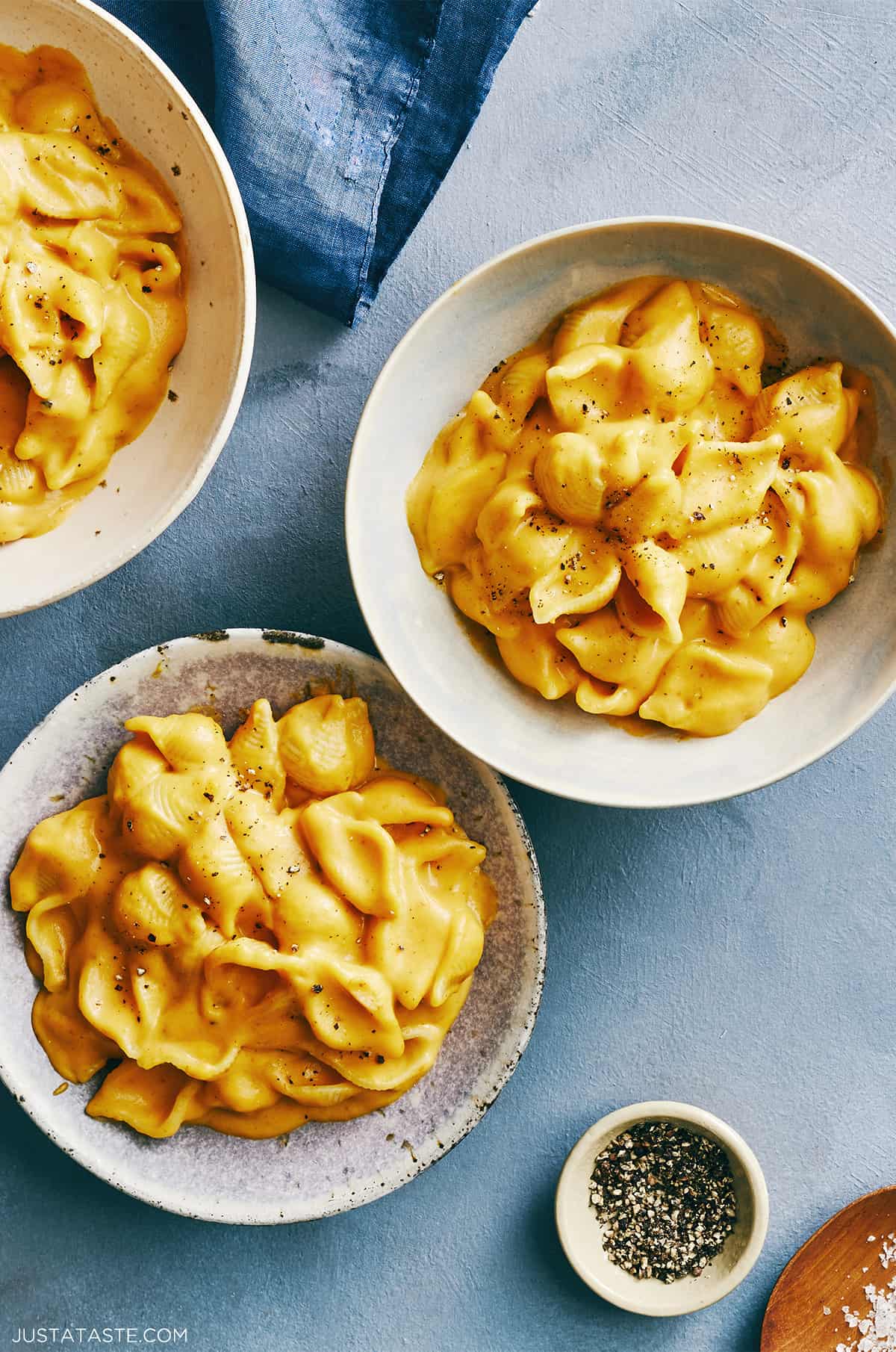 Two bowls containing creamy pumpkin macaroni and cheese next to a small bowl containing black pepper.