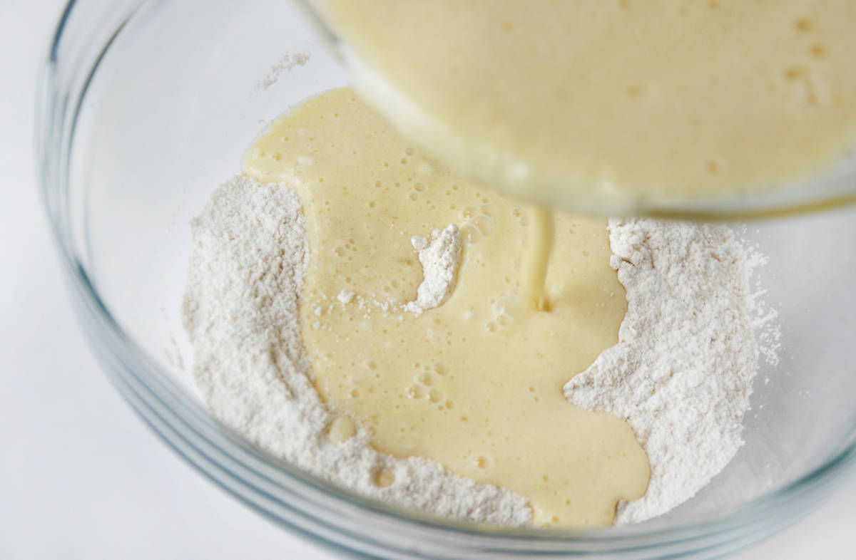 Wet ingredients behind poured from one glass mixing bowl into another glass mixing bowl containing dry ingredients.