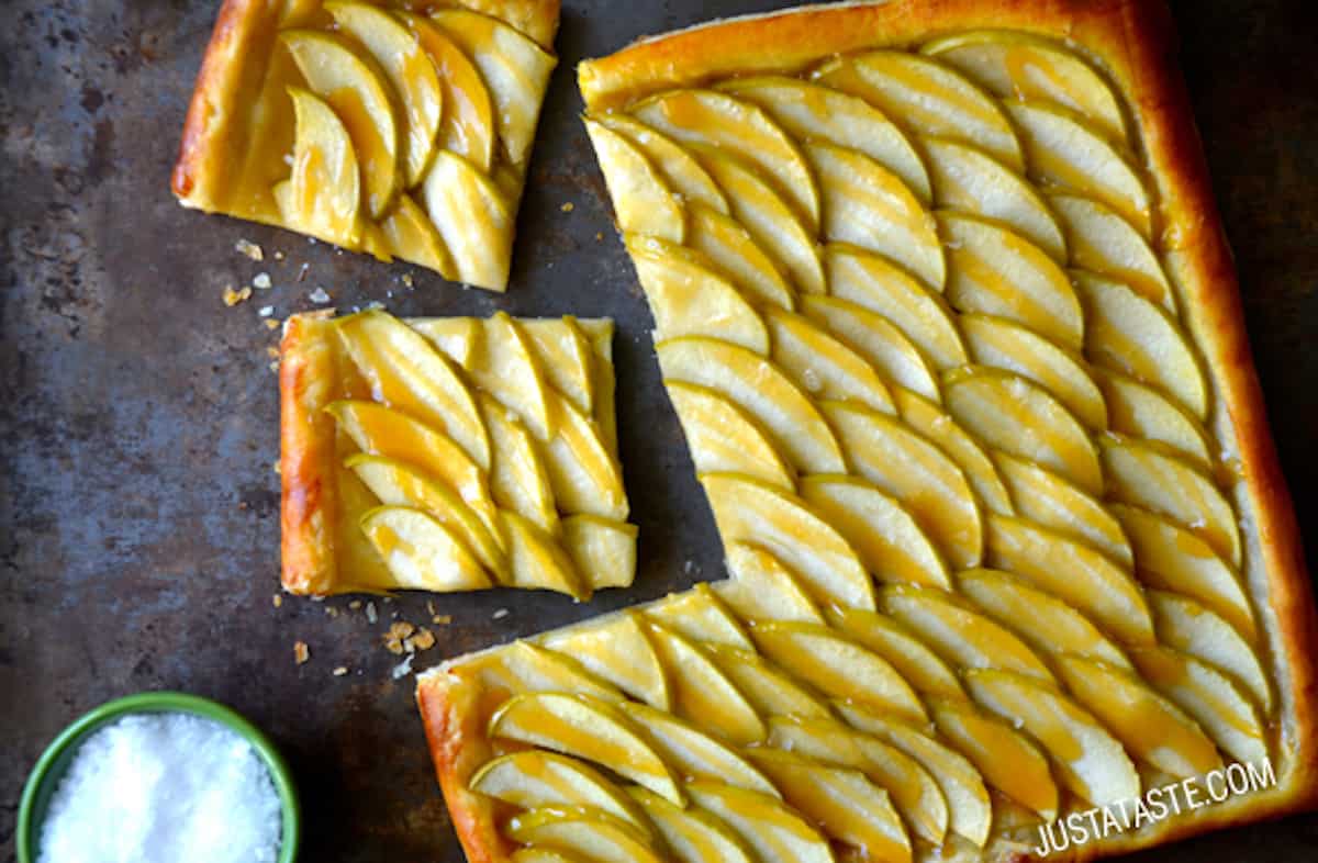 A salted caramel apple tart with two pieces cut off of it and a small bowl of salt beside it.