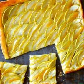 A salted caramel apple tart with two pieces sliced off of it and a small bowl of flakey salt next to it.