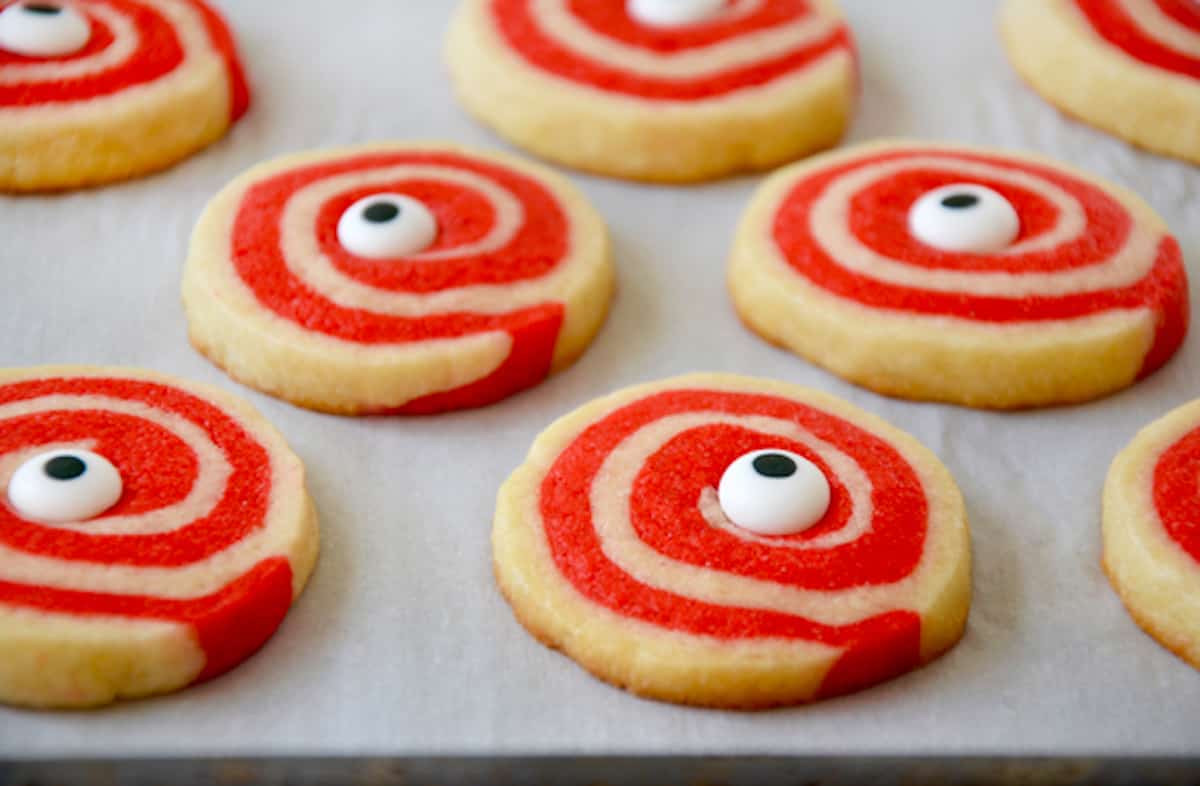 Baked red and white pinwheel cookies with candy eyeballs in their centers on a parchment-lined baking sheet.