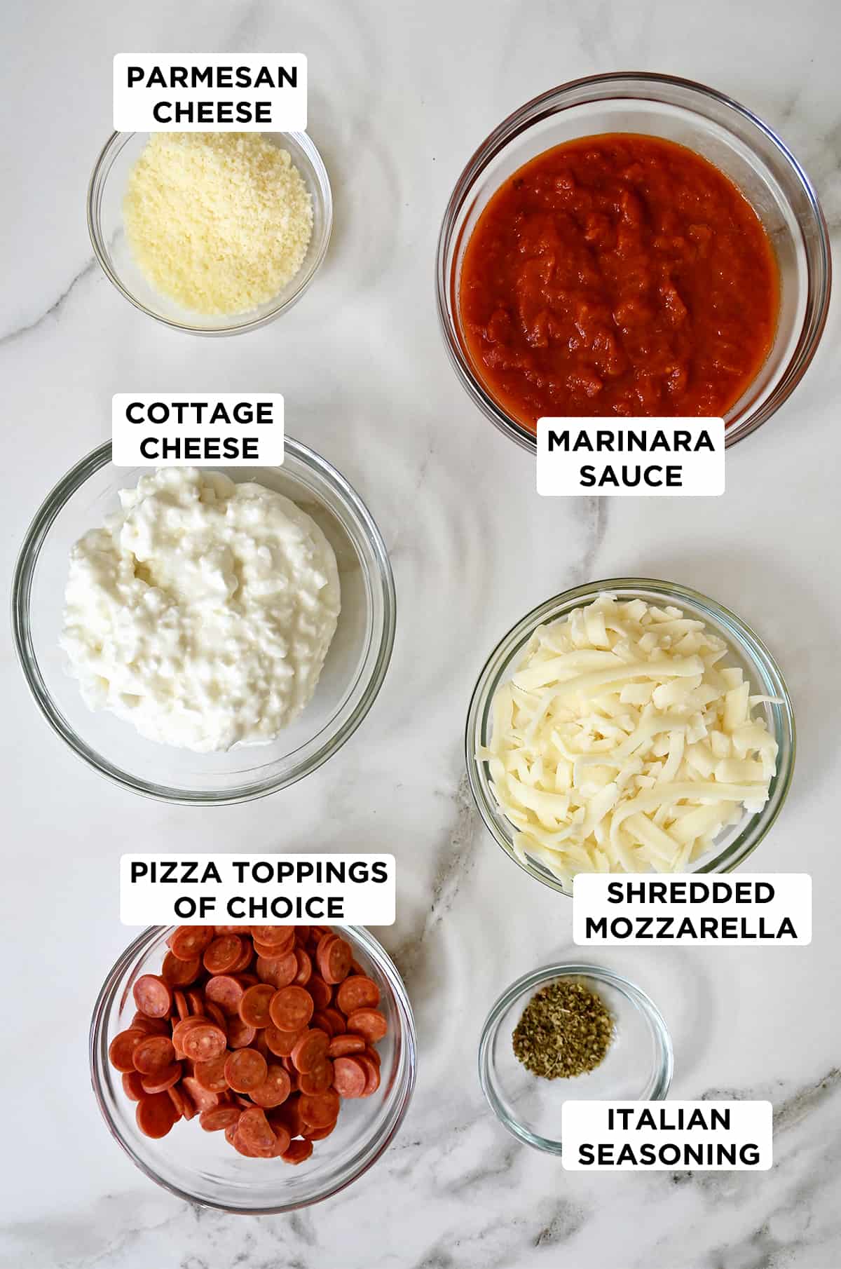 Several clear bowls containing pizza dip ingredients, including cottage cheese, marinara sauce, shredded mozzarella, Italian seasoning, mini pepperoni and grated Parmesan cheese.