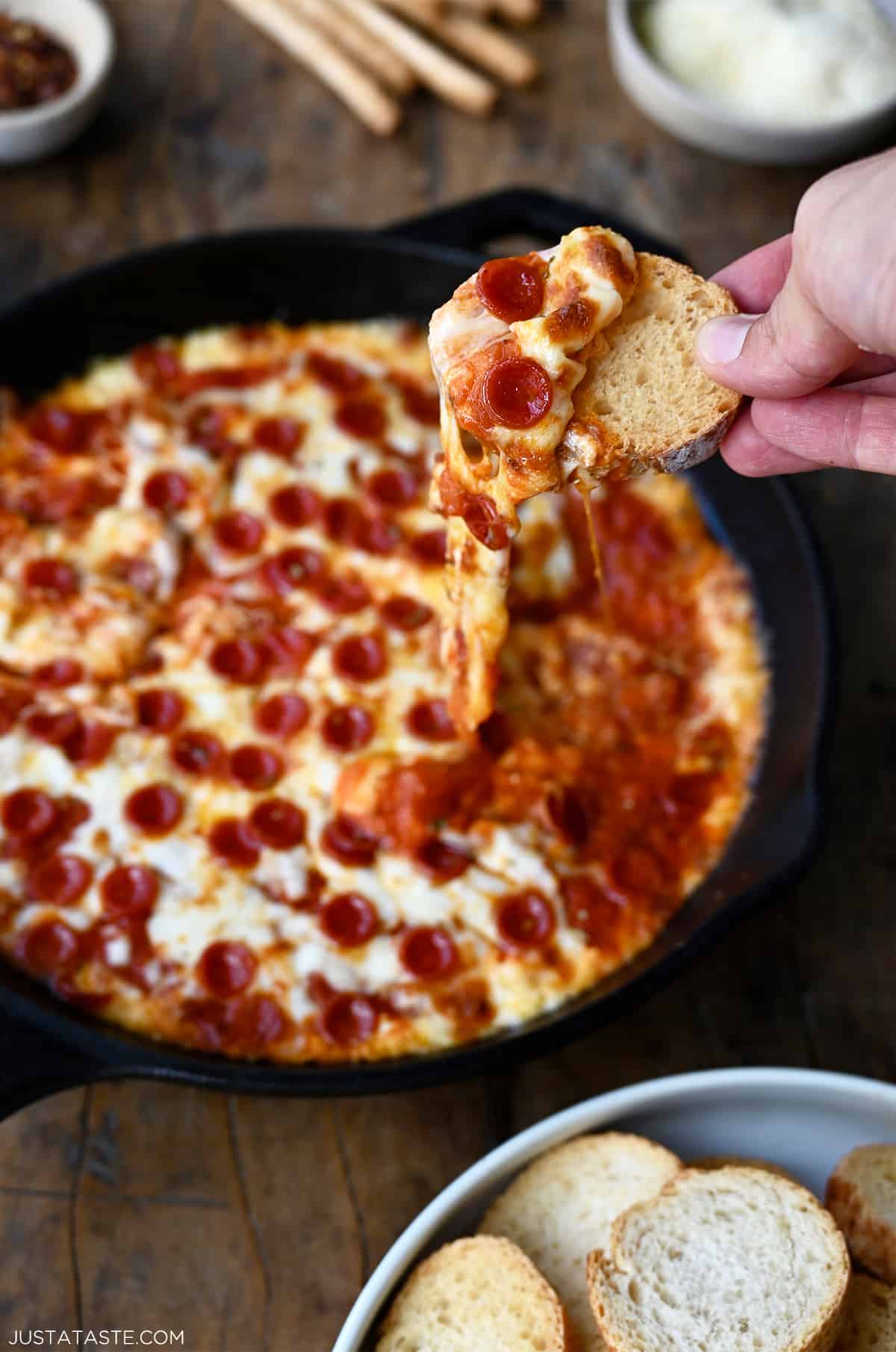 A hand holds a toast that's been dipped into cheesy pizza dip with pepperoni.