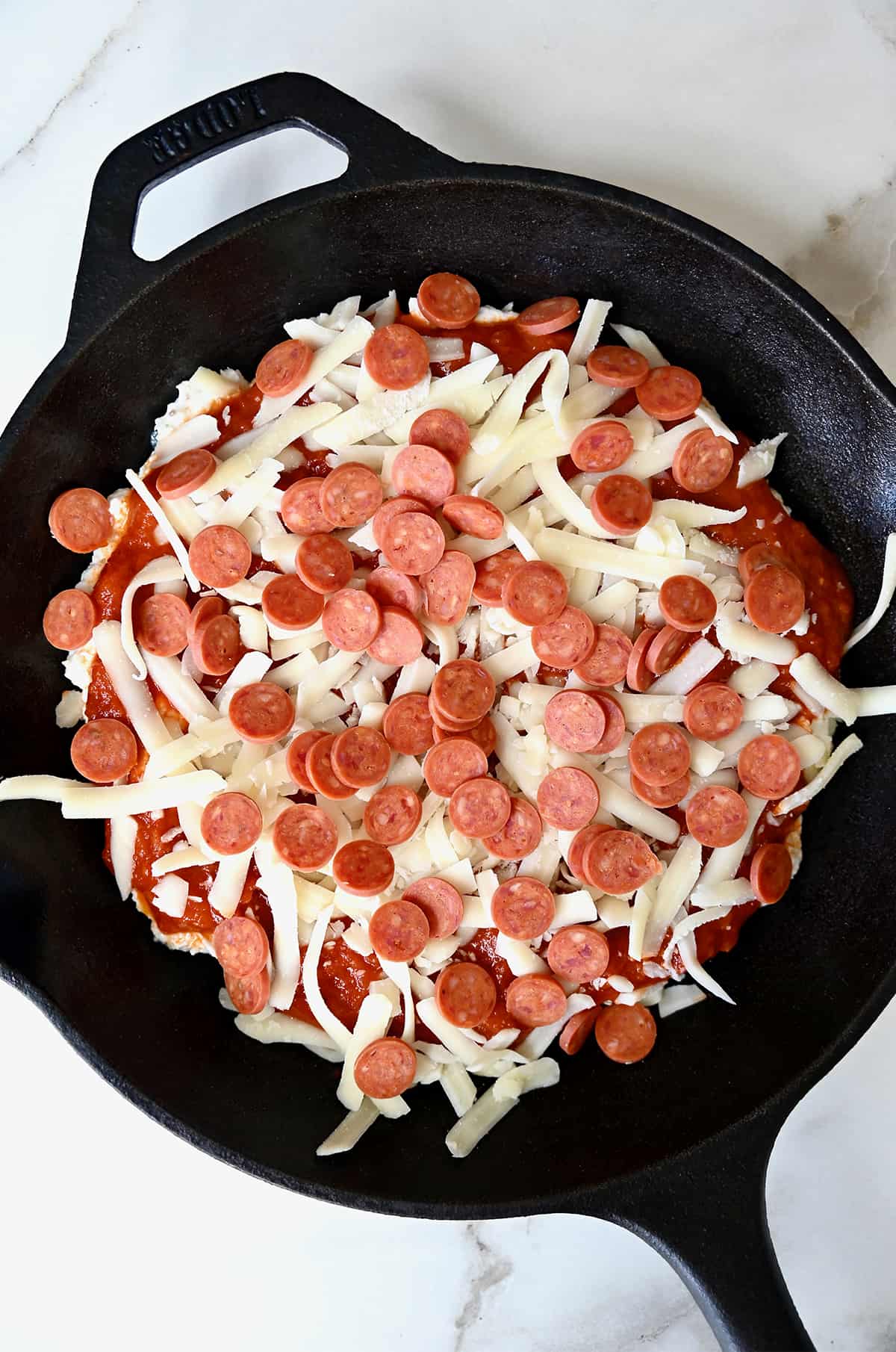 Unbaked pepperoni pizza dip in a cast iron skillet topped with shredded mozzarella cheese.