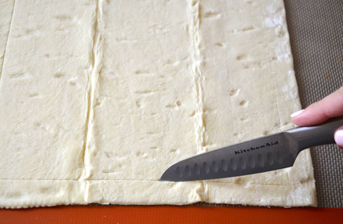 A person using a knife to score a border onto a sheet of puff pastry.