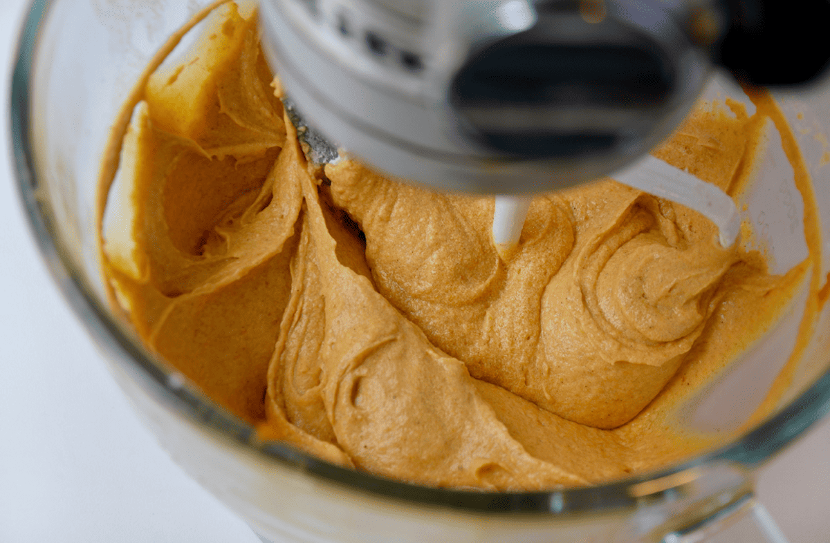 A stand mixer fitted with a paddle attachment and mixing pumpkin bread batter in its bowl.