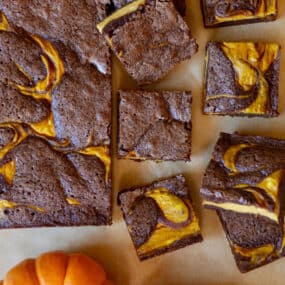Pumpkin cheesecake brownies out of their pan and with several squares of brownies cut off and two small pumpkins beside them.