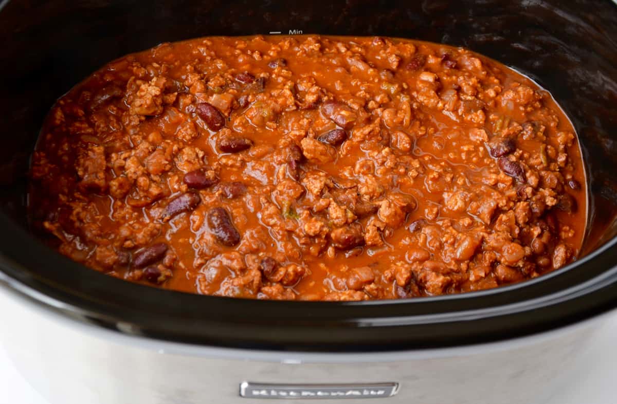 A slower without its lid on cooking ground chicken chili.