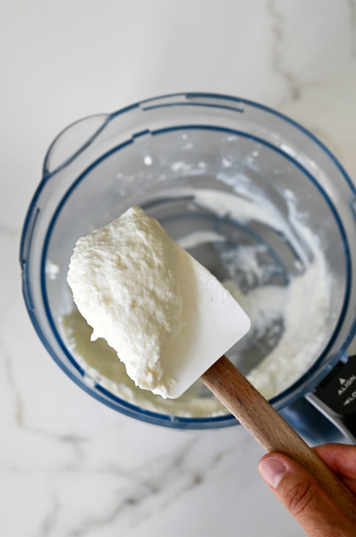 Whipped cottage cheese on a spatula above a food processor.
