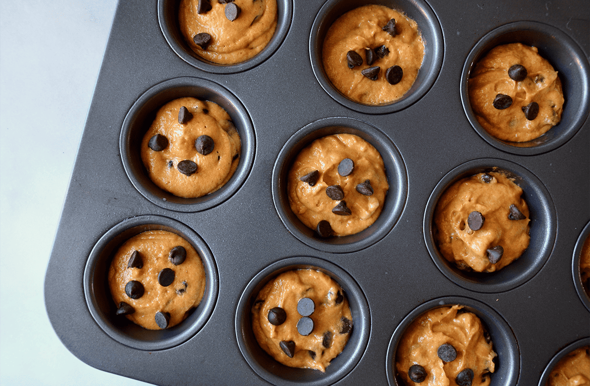 Unbaked pumpkin muffins in a muffin tin with chocolate chips on top.